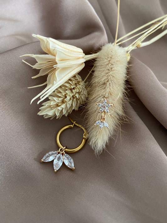 Ensemble de fleurs séchées posées sur un draps en soie rose avec des boucles d'oreilles en acier inoxydable doré. Les boucles d'oreilles ont des pendentifs en fleur de lotus.